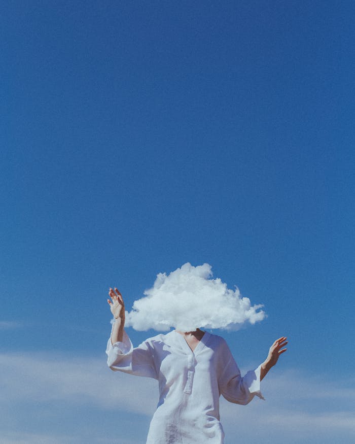 A surreal image of a woman with a cloud covering her head, set against a vibrant blue sky.