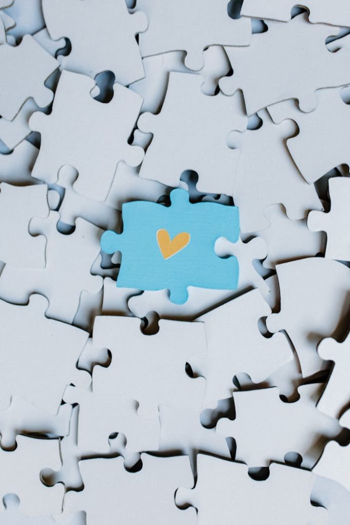 A single blue puzzle piece with a heart stands out in a sea of white pieces.