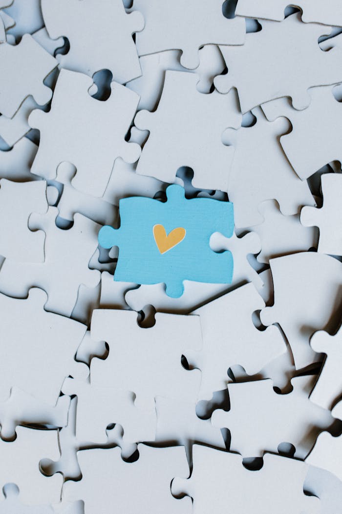 A single blue puzzle piece with a heart stands out in a sea of white pieces.